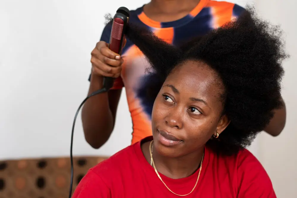 Young woman getting a section of her curly natural hair straightened with a red flat iron