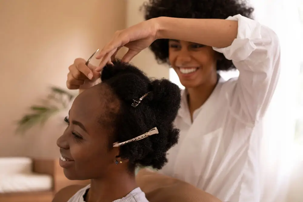 Smiling Afro hairstylist trimming the ends of her client's afro-textured hair with scissors, using hair clips to section the hair.