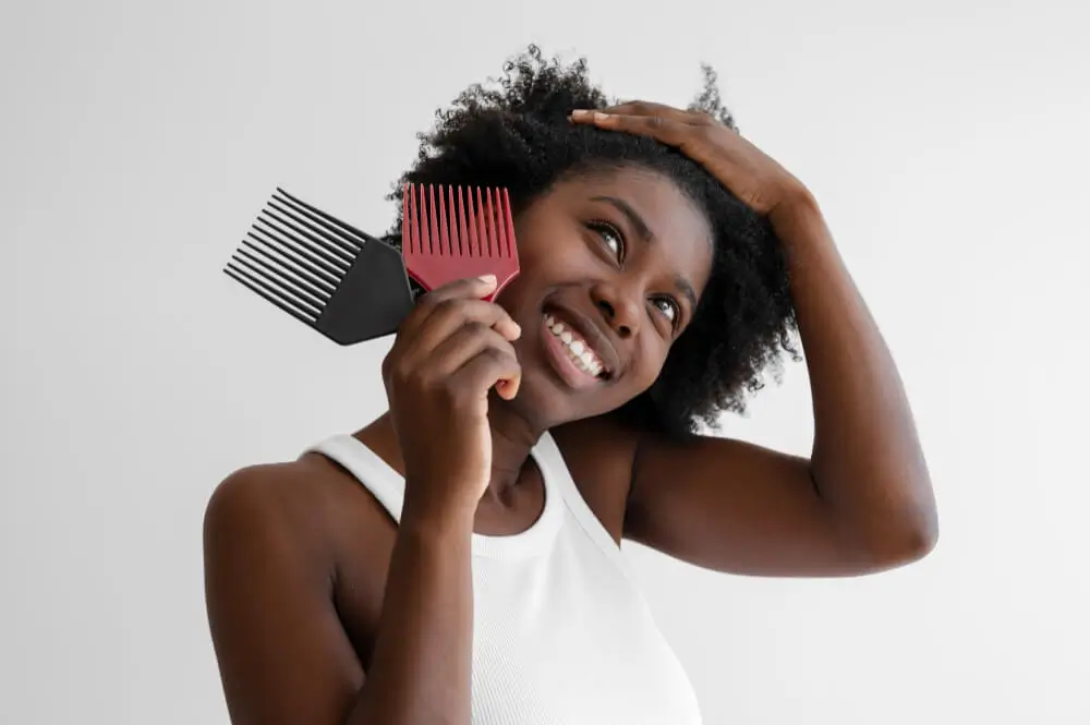 Portrait of a happy, smiling woman with natural afro hair holding a red and a black afro pick.